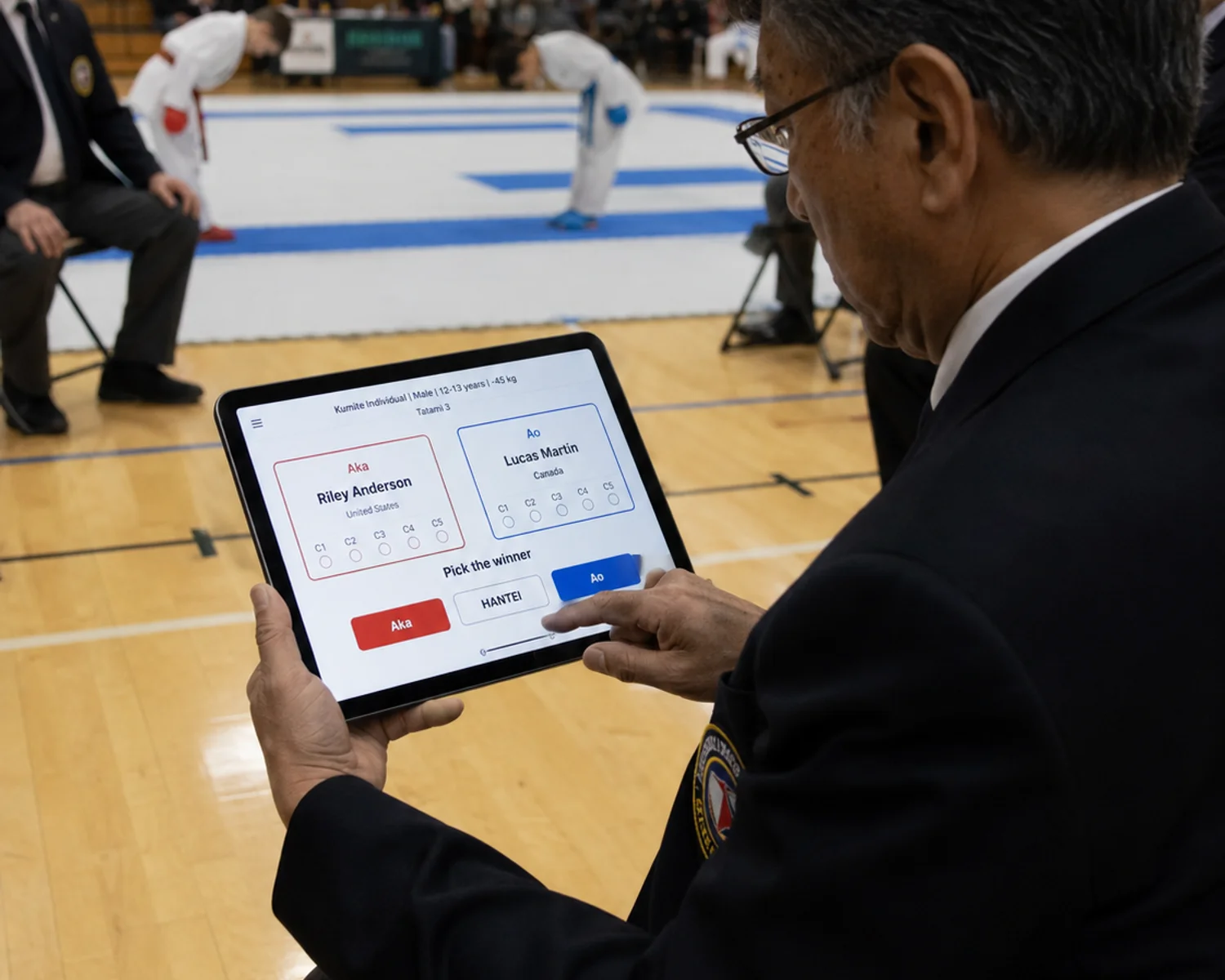 Karate judge at ringside holding a tablet, recording a match result